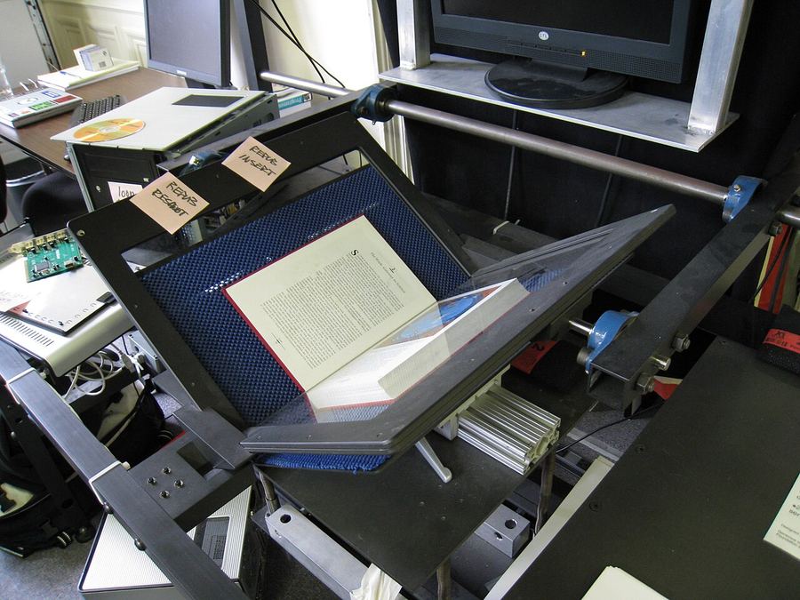 An operator at an Internet Archive book scanner, with a book held open under a glass platen between two cameras